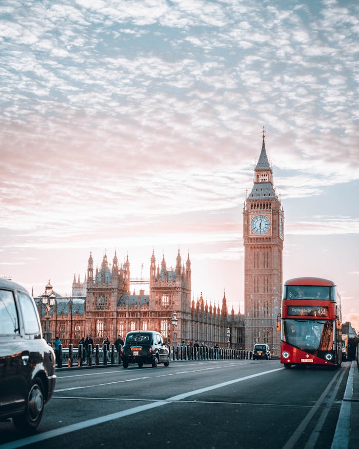 Iconic view of Big Ben and Westminster Bridge at sunset with classic London buses and cars.